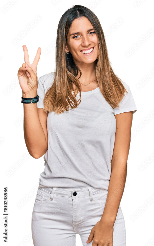 Young woman wearing casual white t shirt smiling with happy face winking at the camera doing victory sign. number two. Young woman wearing casual white t shirt smiling with happy face winking at the camera doing victory sign. number two.