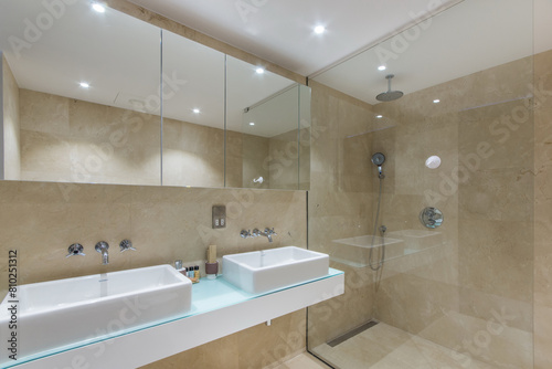 The hotel s bathroom is decorated with beige tiles  with a shower cabin and a large mirror.