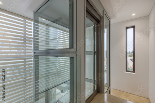 The corridor of a Mediterranean villa with light walls, a window and a glass elevator.