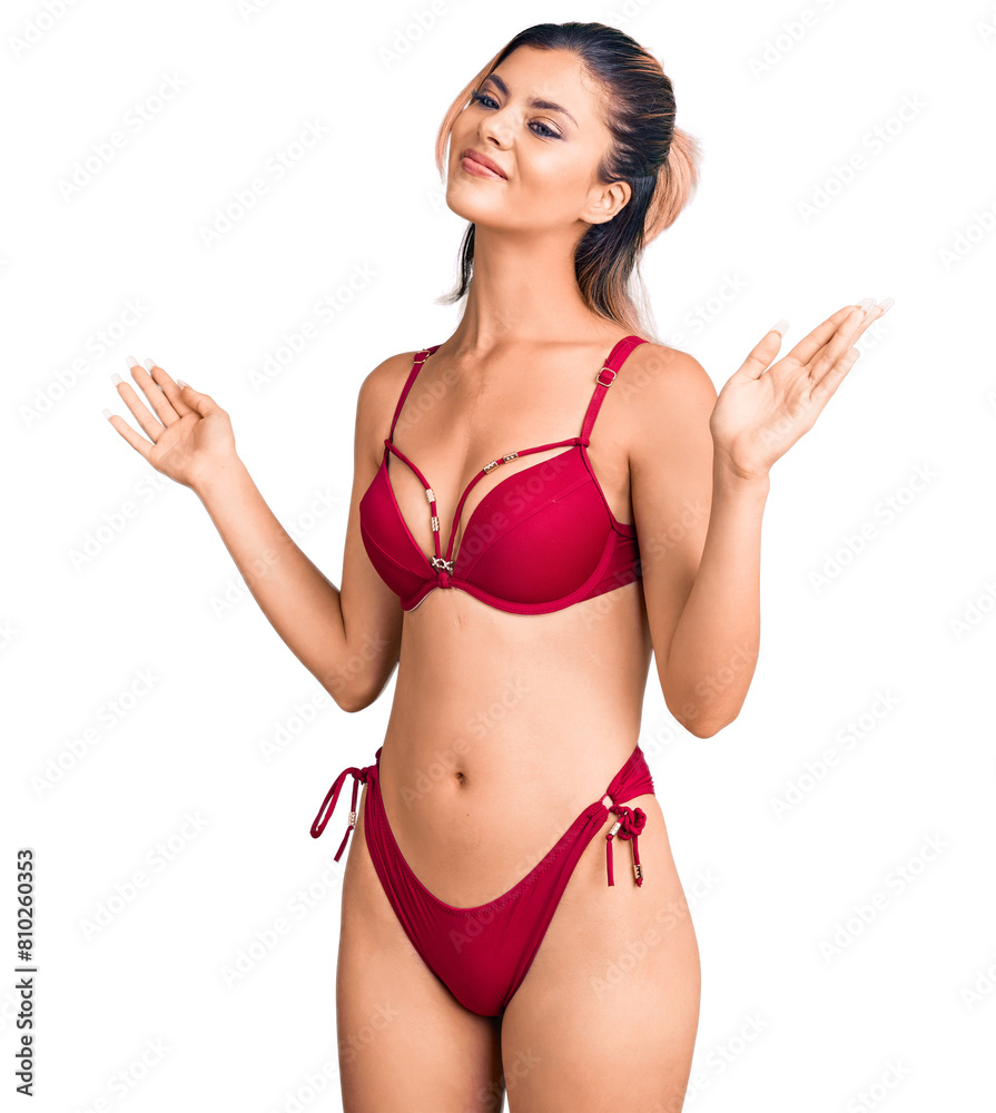 Young beautiful woman wearing bikini clueless and confused expression with arms and hands raised. doubt concept. Young beautiful woman wearing bikini clueless and confused expression with arms and hands raised. doubt concept.