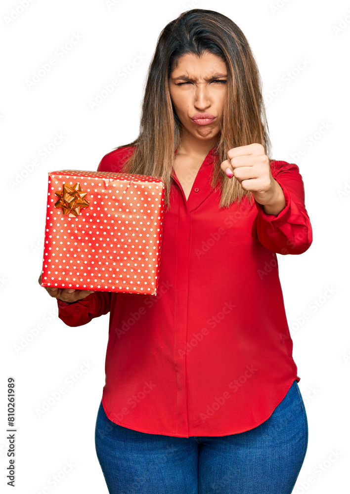 Beautiful brunette woman holding gift annoyed and frustrated shouting with anger, yelling crazy with anger and hand raised Beautiful brunette woman holding gift annoyed and frustrated shouting with anger, yelling crazy with anger and hand raised