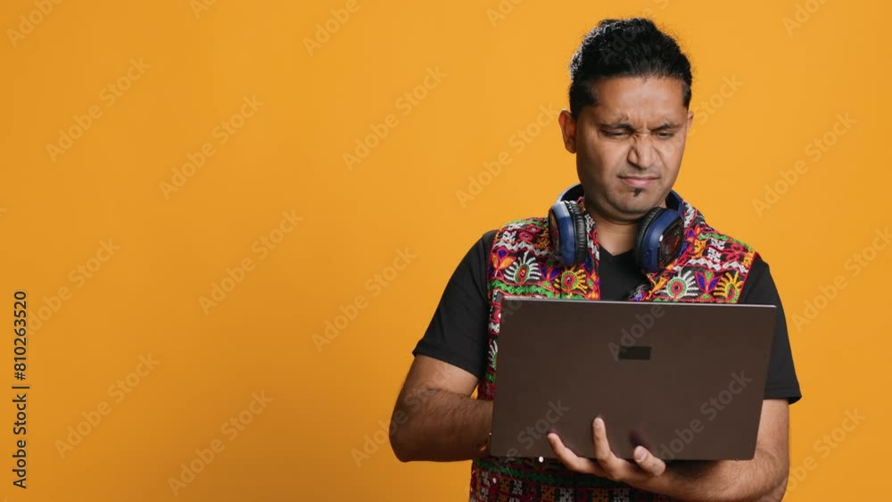 Indian man composing email, typing on laptop, frustrated with malfunctioning keyboard. Person sending mail online, struggling to use defective notebook, studio background, camera A