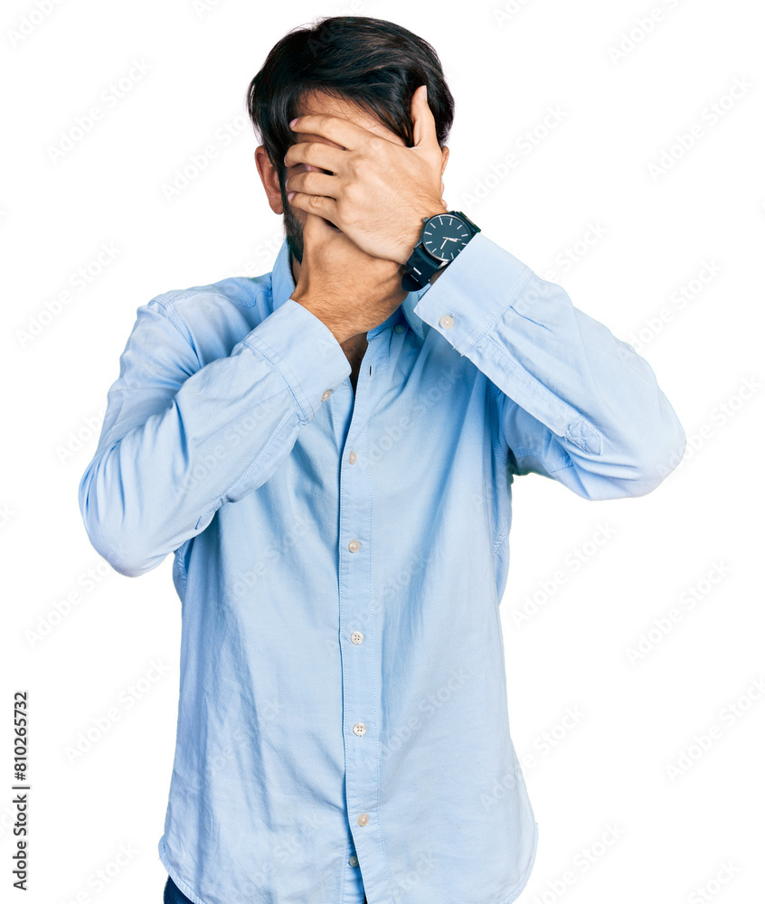 Hispanic man with blue eyes wearing business shirt covering eyes and mouth with hands, surprised and shocked. hiding emotion Hispanic man with blue eyes wearing business shirt covering eyes and mouth with hands, surprised and shocked. hiding emotion