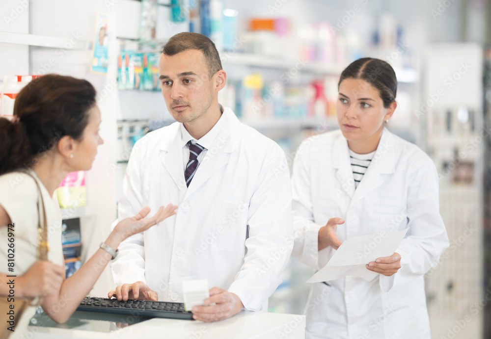 Man and woman pharmacists looking for prescription medicine for adult woman using computer