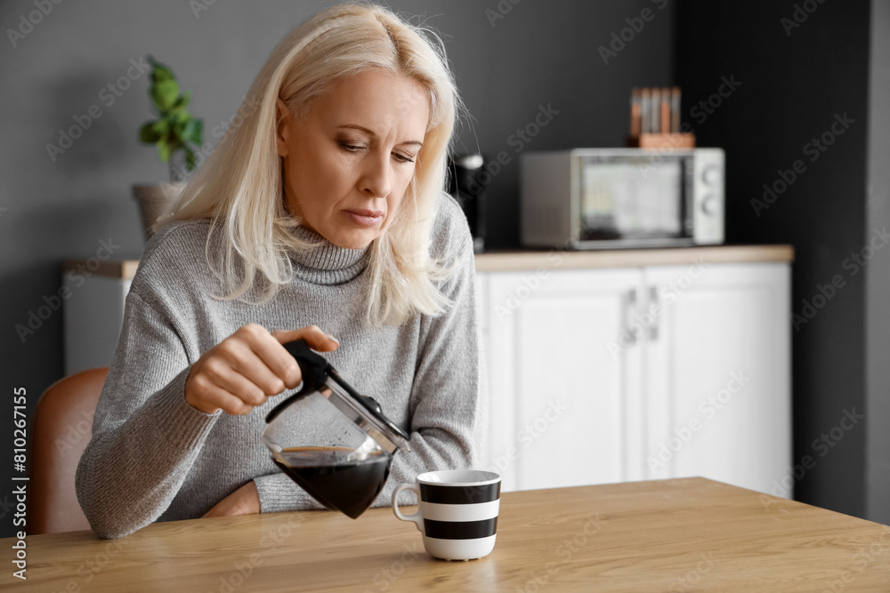 Depressed mature woman pouring coffee in kitchen