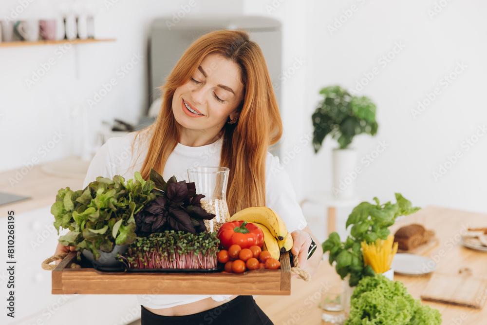 Happy sporty mature woman smiling with braces and holding tray with healthy food in kitchen at home