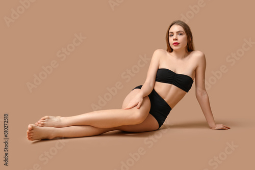 Beautiful young woman in black underwear sitting against beige background © Pixel-Shot