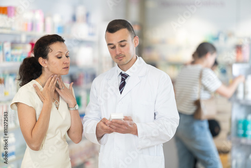 Woman talking with male doctor in chemist shop about her pain in neck. Pharmacist offering tratment to her