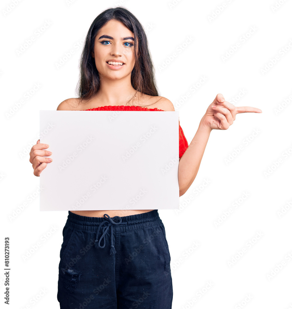 Brunette teenager girl holding blank empty banner smiling happy pointing with hand and finger to the side Brunette teenager girl holding blank empty banner smiling happy pointing with hand and finger to the side