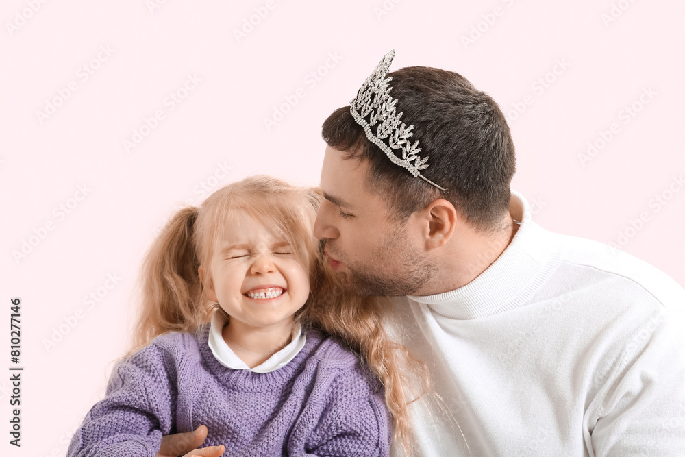 Happy father and his cute little daughter in princess crowns on pink background Happy father and his cute little daughter in princess crowns on pink background