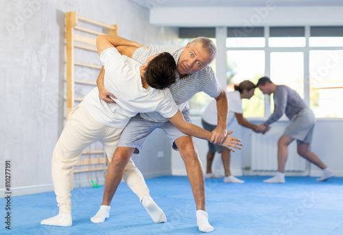 Young guy and elderly men training judo techniques in studio..