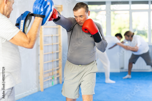 Adult man is training with coach and punching gloves in box gym - hits punch mitts photo