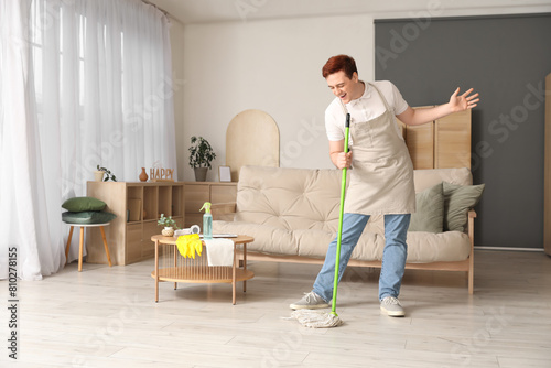 Young man singing while mopping floor in living room © Pixel-Shot