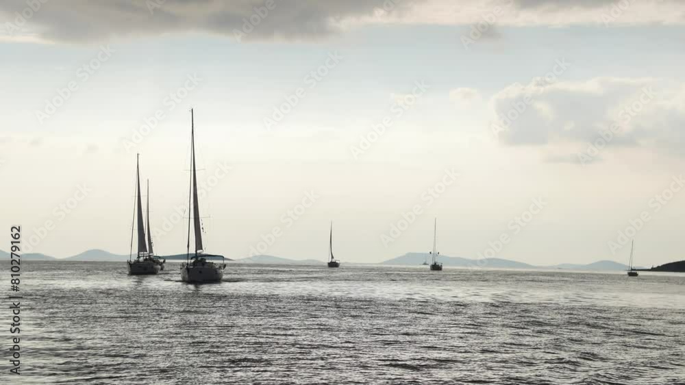 A group of sailboats are sailing in the ocean. The sky is cloudy and the water is calm A group of sailboats are sailing in the ocean. The sky is cloudy and the water is calm