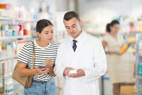 Polite male pharmacist consulting young girl about medicament in box in chemist's shop photo