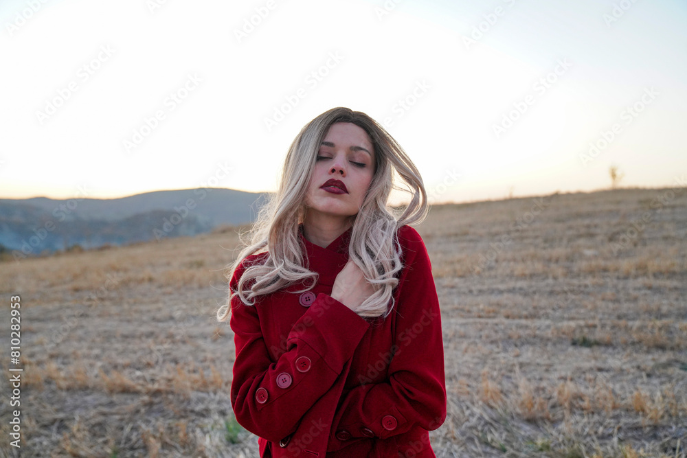 A blonde woman with red clothing is standing in a field. Emotional and aesthetic portrait of a beautiful blonde woman A blonde woman with red clothing is standing in a field. Emotional and aesthetic portrait of a beautiful blonde woman