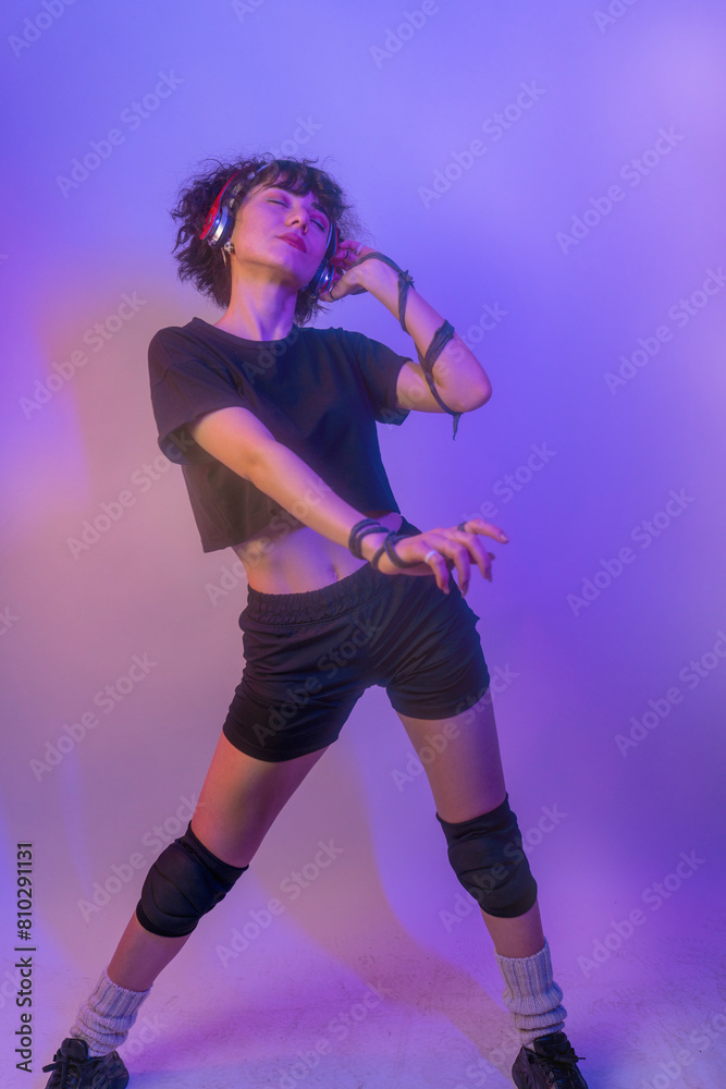 A woman is dancing and wearing headphones. She is smiling and she is enjoying herself. young woman listening to music on colorful background A woman is dancing and wearing headphones. She is smiling and she is enjoying herself. young woman listening to music on colorful background
