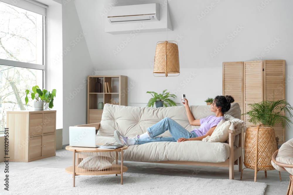 Young African-American woman turning on air conditioner at home Young African-American woman turning on air conditioner at home