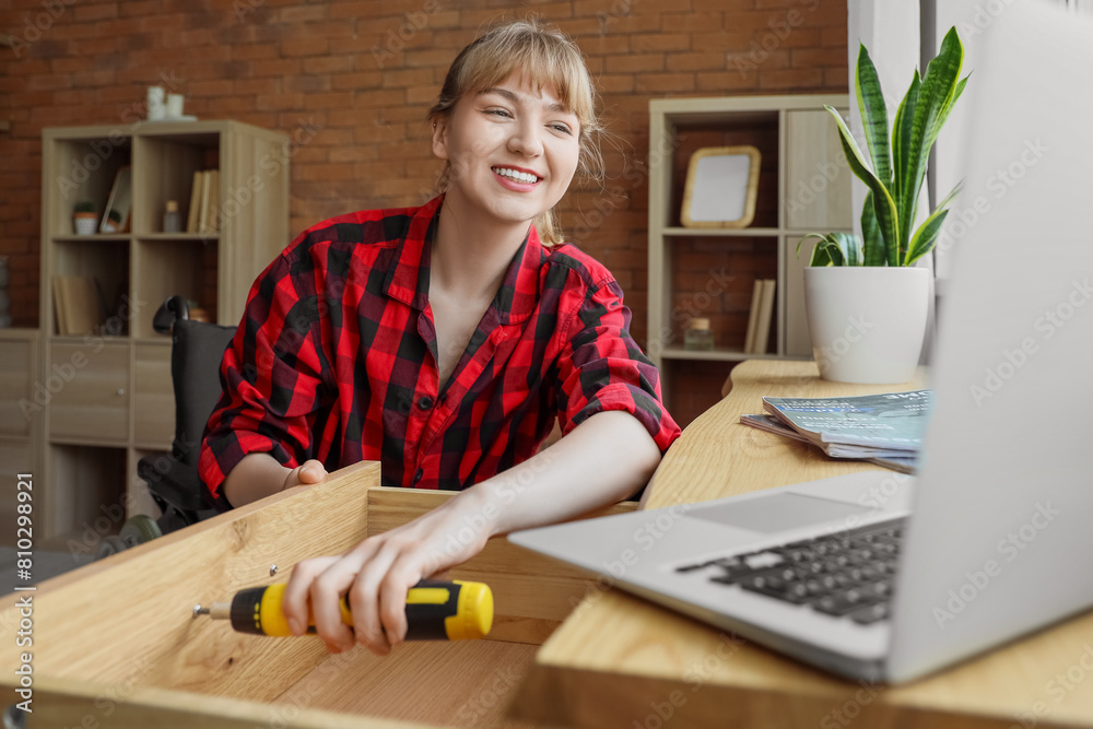 Young woman in wheelchair with laptop repairing drawer at home Young woman in wheelchair with laptop repairing drawer at home