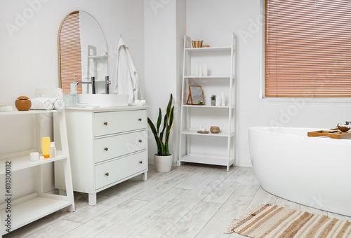 Interior of light bathroom with bathtub  chest of drawers and houseplant