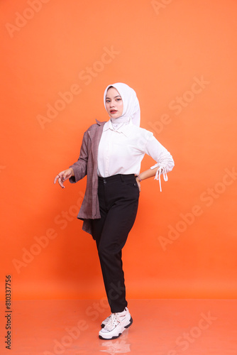 Full length portrait of beautiful elegant Muslim Asian woman model holding buttocks and front wearing half white office wear hijab isolated orange studio background. Concept of fashion, beauty
