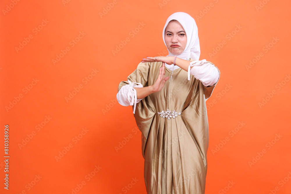 expression of beautiful adult indonesia woman frowning hands stop sign wearing kaftan muslim dress with hijab, isolated on orange background. Concept of fashion, education, promotion