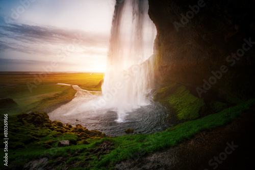 Sunlight beams through a cascading waterfall in a tranquil landscape at dusk