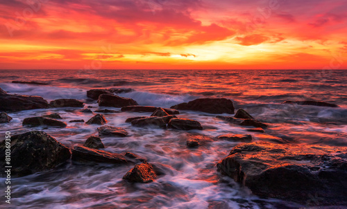 Vibrant sunset paints the sky above a rocky shoreline with crashing waves