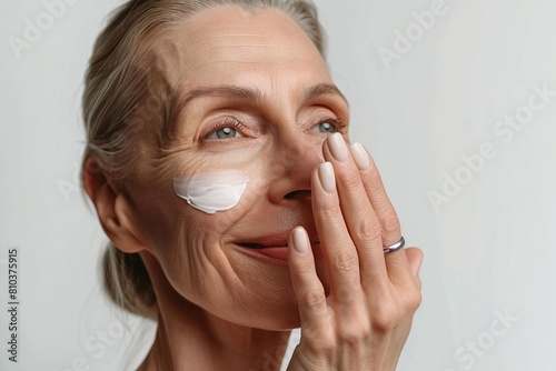 gray-haired old woman smears her face with cream, on a gray background