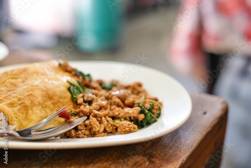 A plate of pad kra pao (holy basil pork mince stir-fry) with omelette and mixed grain rice at Thong Heng Lee, a family-run street food restaurant near the Grand Palace in Bangkok, Thailand