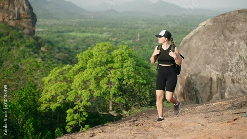 Active woman hikes up rocky trail with Sigiriya Rock in distance. Female adventurer in fitness gear explores Sri Lanka, breathes fresh air atop Pidurangala Rock, rich scenery, feels nature peace.
