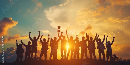 Success of teamwork. Winning team is holding trophy in hands. Silhouettes of many hands in sunset photo