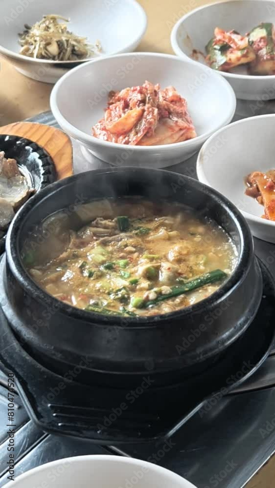 Boiling soy bean paste soup, a dish in Korean food together with other side dishes on table in a restaurant. High angle view. Vertical format.