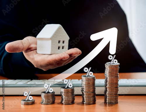 Home tax concept, residential or real estate property annual taxation, profit from sales concept. Rising arrow and percentage icon on coin stack graph steps and man holding white small house in hand.