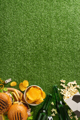 Assortment of game day snacks including burgers, chips, popcorn, and beer, staged on a green vertical textured background to simulate a football field