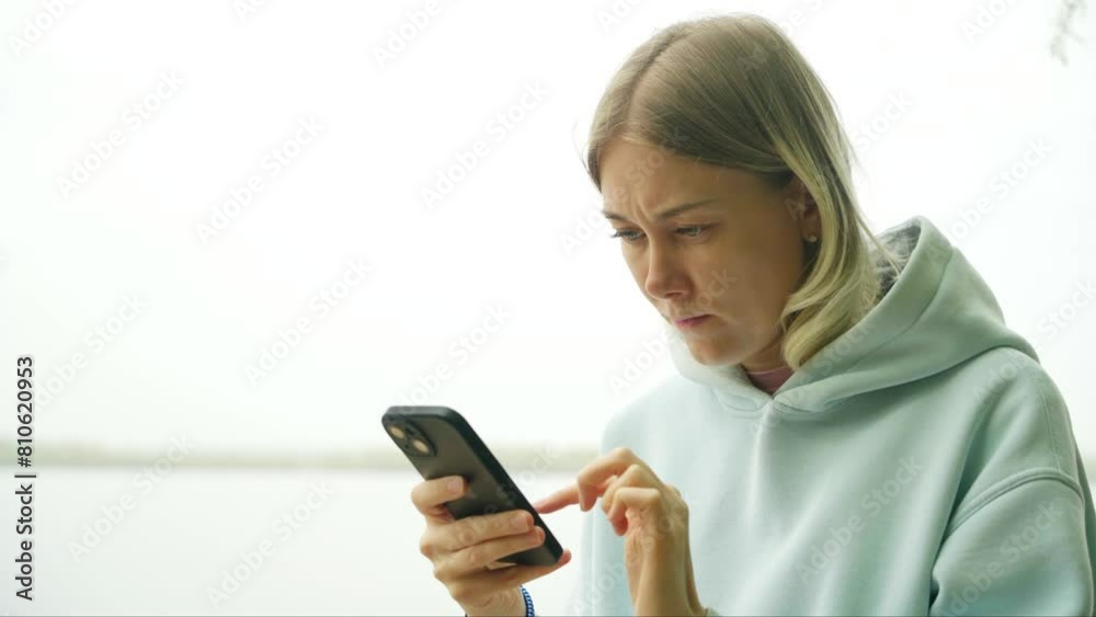 A beautiful adult girl with a cute face uses a mobile phone on the river bank. A young woman communicates on social networks while walking outdoors. Healthy and active lifestyle. A beautiful adult girl with a cute face uses a mobile phone on the river bank. A young woman communicates on social networks while walking outdoors. Healthy and active lifestyle.