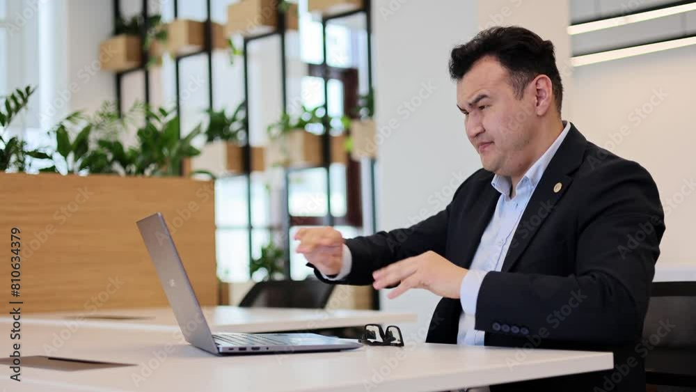 Asian businessman earnestly works at his laptop, then stares into the camera Asian businessman earnestly works at his laptop, then stares into the camera