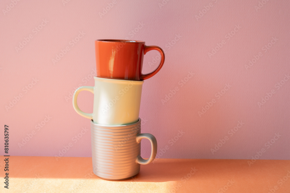 Stack of mug cups on orange shelf. pink wall background
