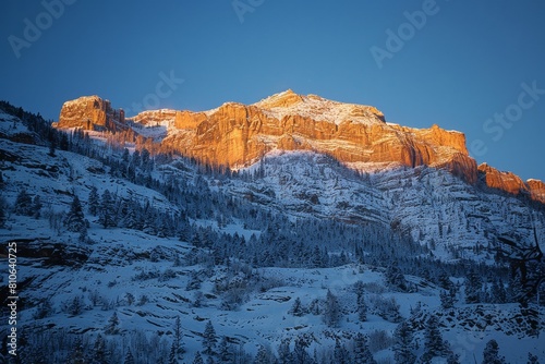 Golden sunrise illuminates snow-capped mountain peaks in a stunning alpine winter landscape. Majestic scenery, untouched nature, and serene wilderness captured in this photograph. 