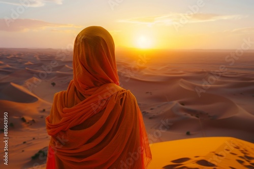 Person draped in orange cloth watching sunset over desert, capturing a moment of awe and contemplation.