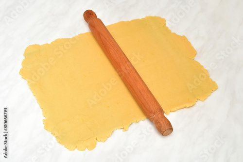 Wooden rolling pin and rolled out dough for pie or cookies on the light gray marble table texture. Selective focus. 
 
