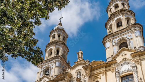 An old colonial building in the historic quarter of Buenos Aires. The Church of San Pedro Gonzalez Telmo. Towers with bells, crosses, sculptures, arches, ornaments against the blue sky and clouds. photo