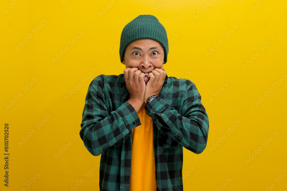Embarrassed young Asian man bites his fingers while looking at the camera, displaying shock, insecurity, anxiety, frustration, confusion, and fear about work related problems. Embarrassed young Asian man bites his fingers while looking at the camera, displaying shock, insecurity, anxiety, frustration, confusion, and fear about work related problems.