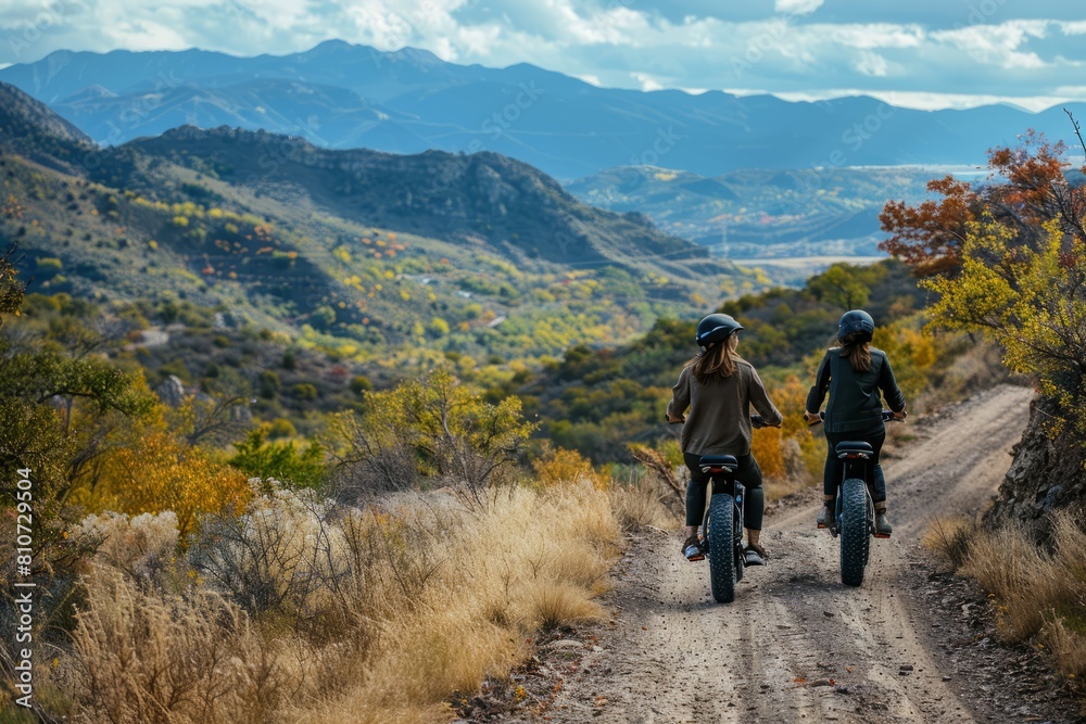 A couple is riding side by side on electric bikes down a dirt road in a mountainous area