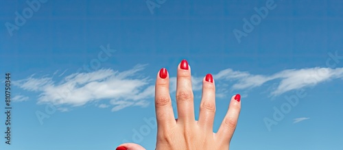 A woman s hand adorned with red painted nails and a black ring on the pinky finger reaches out into the vast expanse of a blue sky creating a beautiful copy space image 200 characters © HN Works