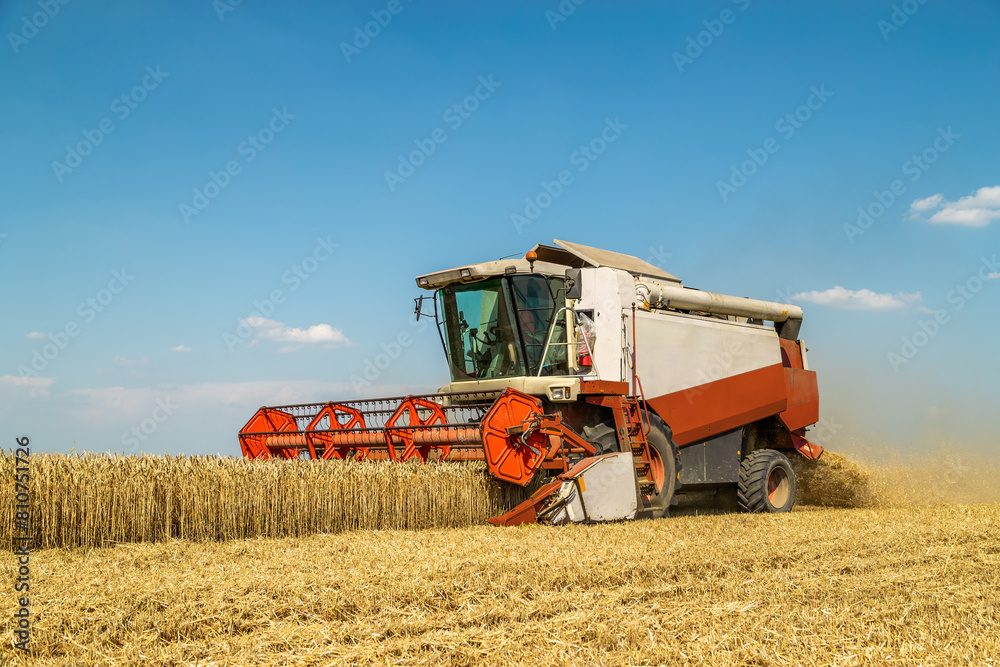 Combine harvester at work under the clear blue sky during wheat harvest season Combine harvester at work under the clear blue sky during wheat harvest season