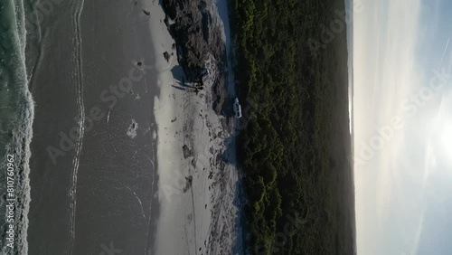Vehicle traveling near the seashore with white sand in Wylie Bay Rock Beach, vertical aerial photo