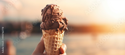 A person holding an ice cream cone with chocolate ice cream set against a blurred background This milk dessert is perfect to enjoy on a summer vacation It features a blank space making it ideal for d photo
