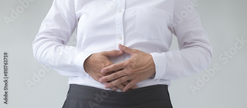 A man wearing a white shirt and black pants stands with a stomach ache his hands clasped tightly to his abdomen The image features a white background with a copy space in front