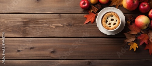 Autumn themed setup with a pie featuring apples a cup of coffee and a notepad placed on a wooden table adorned with dry leaves providing a perfect copy space image